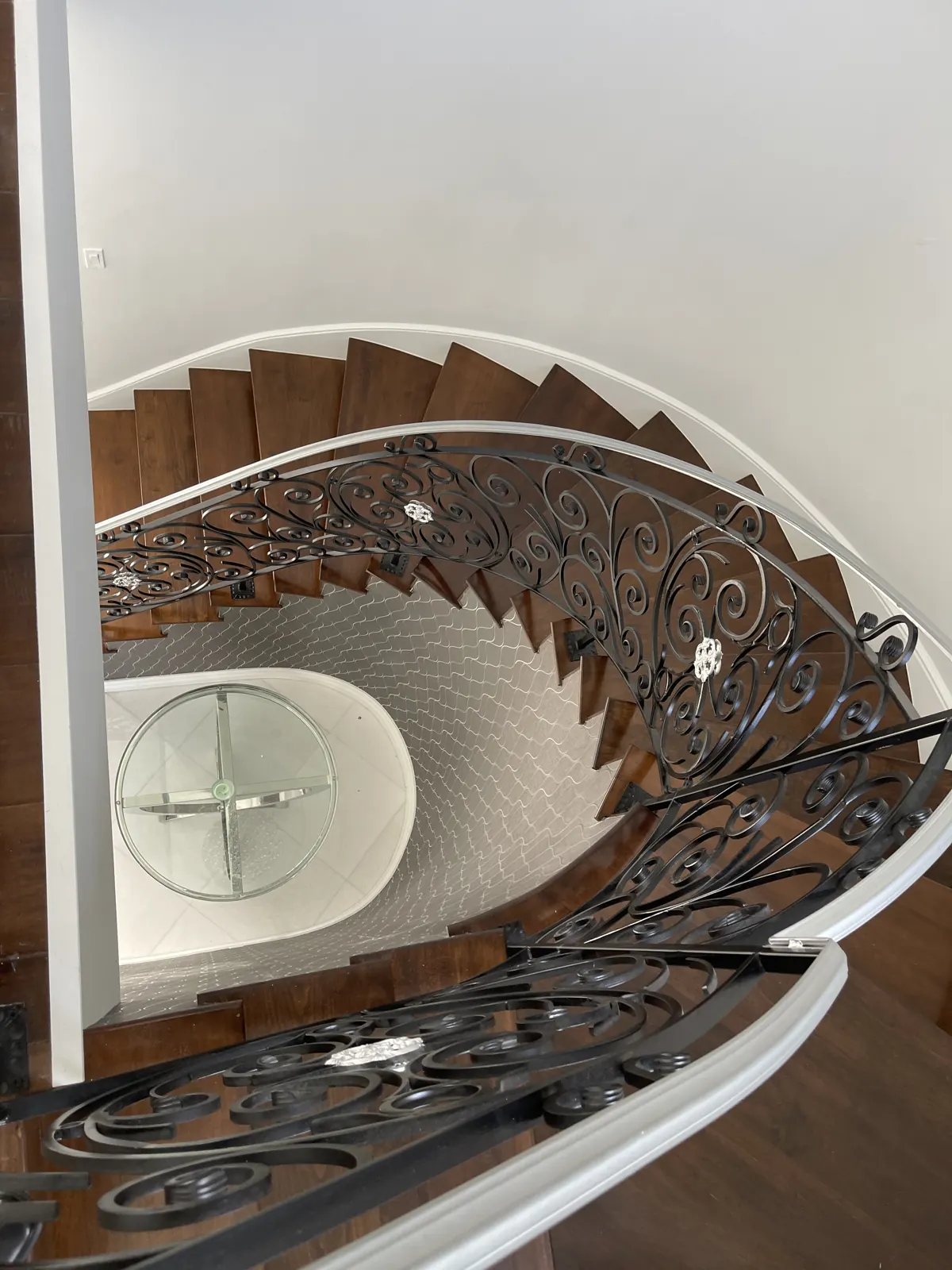 Custom spiral staircase with wood treads and a wrought-iron scroll railing completed by Apadana Group Inc.